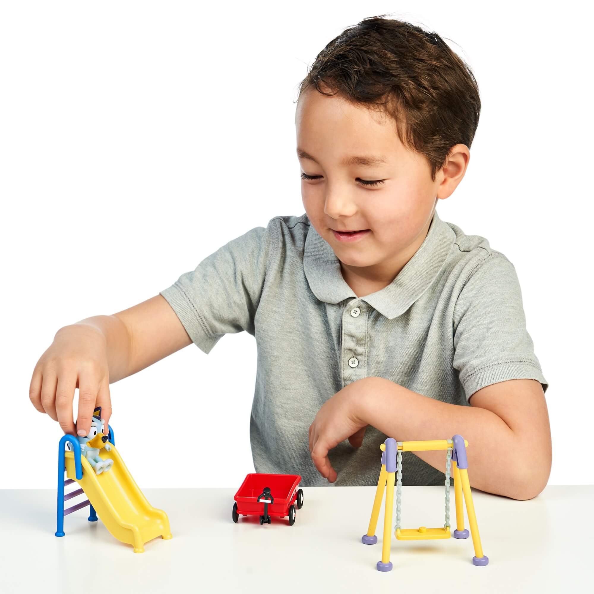 Chłopiec bawi się zestawem Bluey Mini Park z figurką i elementami placu
